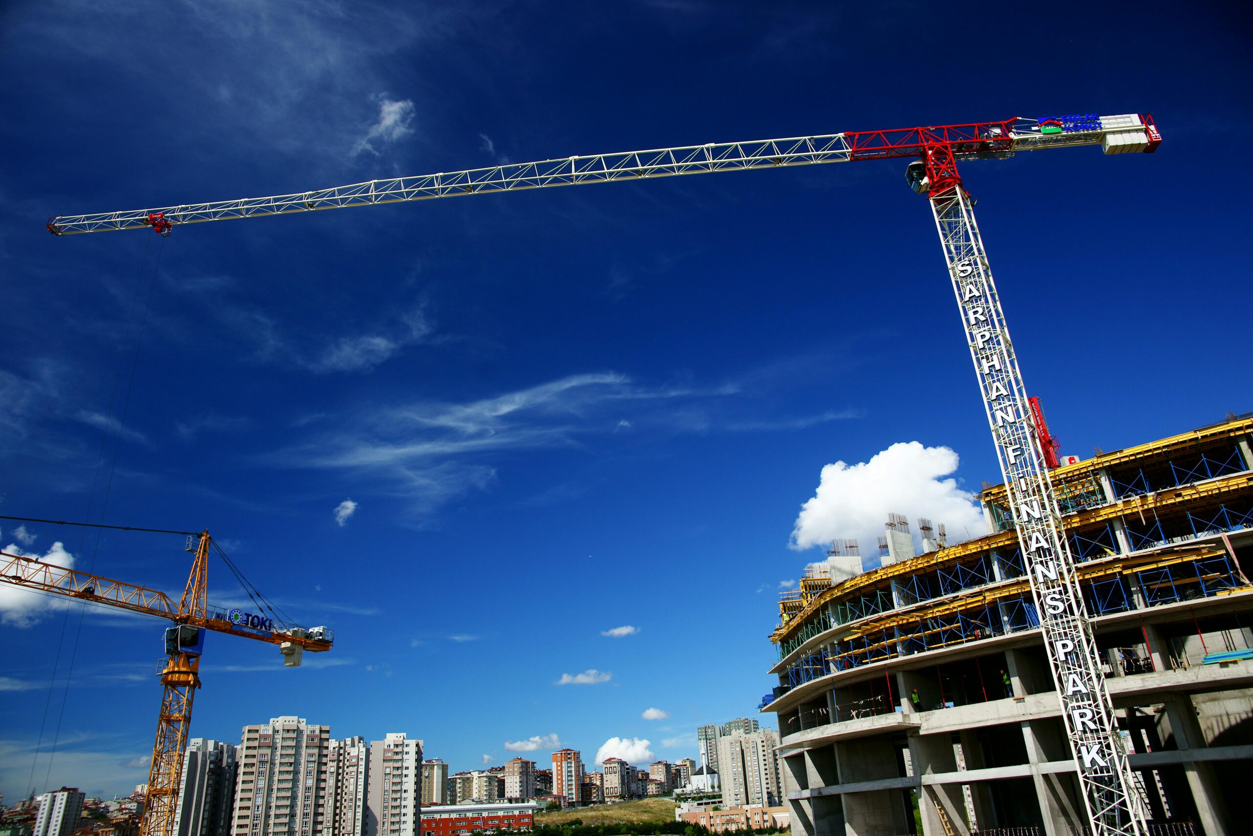 A construction crane looms above a construction site under a blue sky.