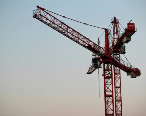 Two construction cranes against a colorful blue sky.