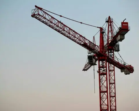 Two construction cranes against a colorful blue sky.