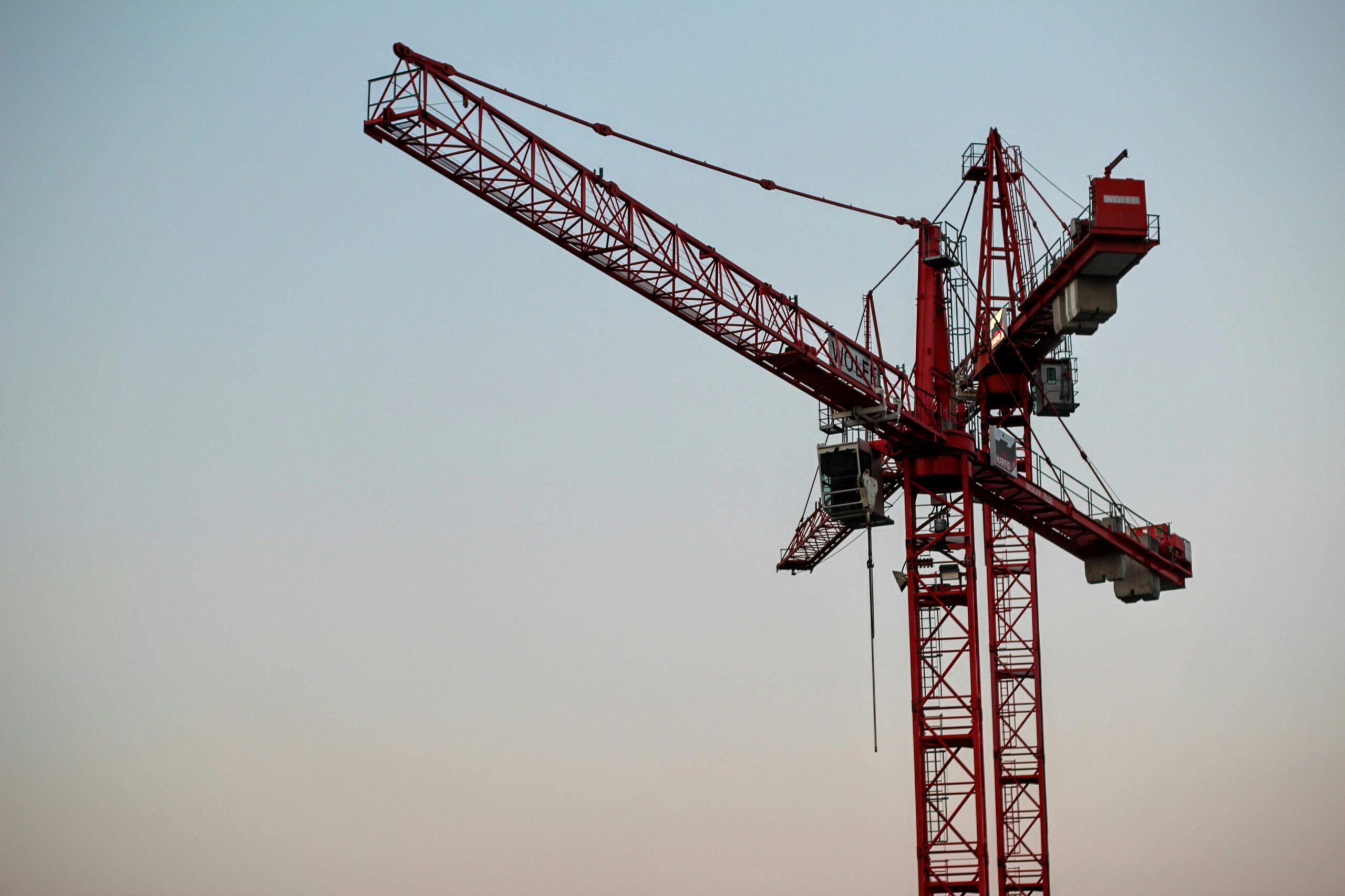 Two construction cranes against a colorful blue sky.