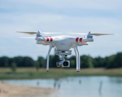 A drone is pictured above a small body of water and trees in the distance.