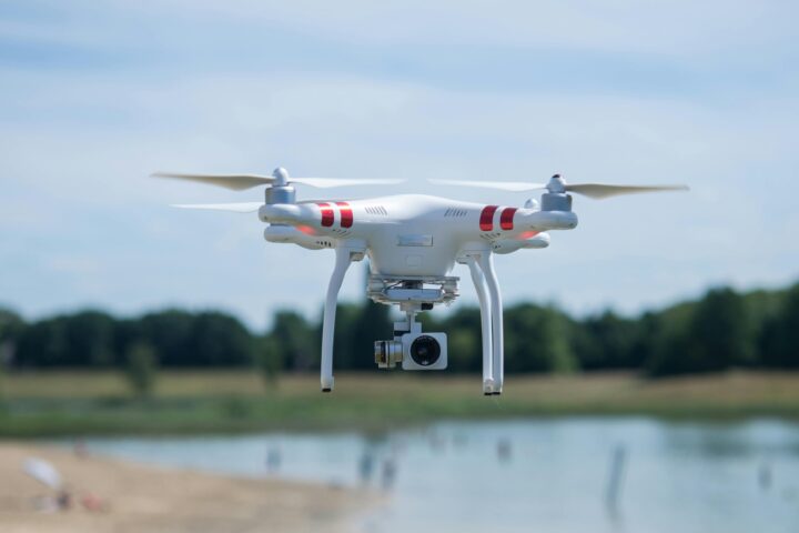 A drone is pictured above a small body of water and trees in the distance.