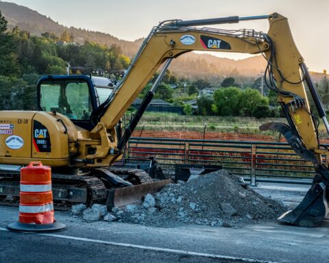 An excavator pulls rumble alongside a concrete road.