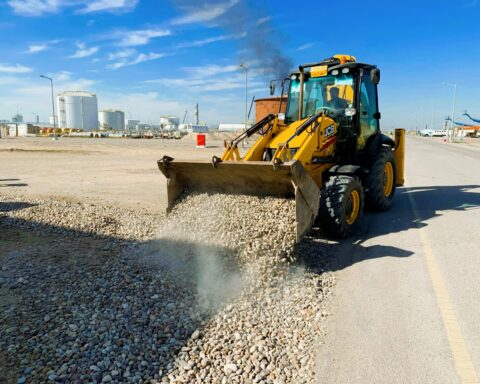An excavator offloads rubble near a road.