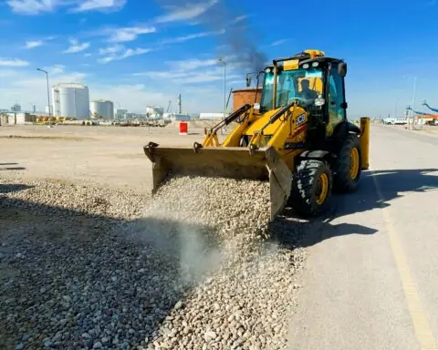 An excavator offloads rubble near a road.