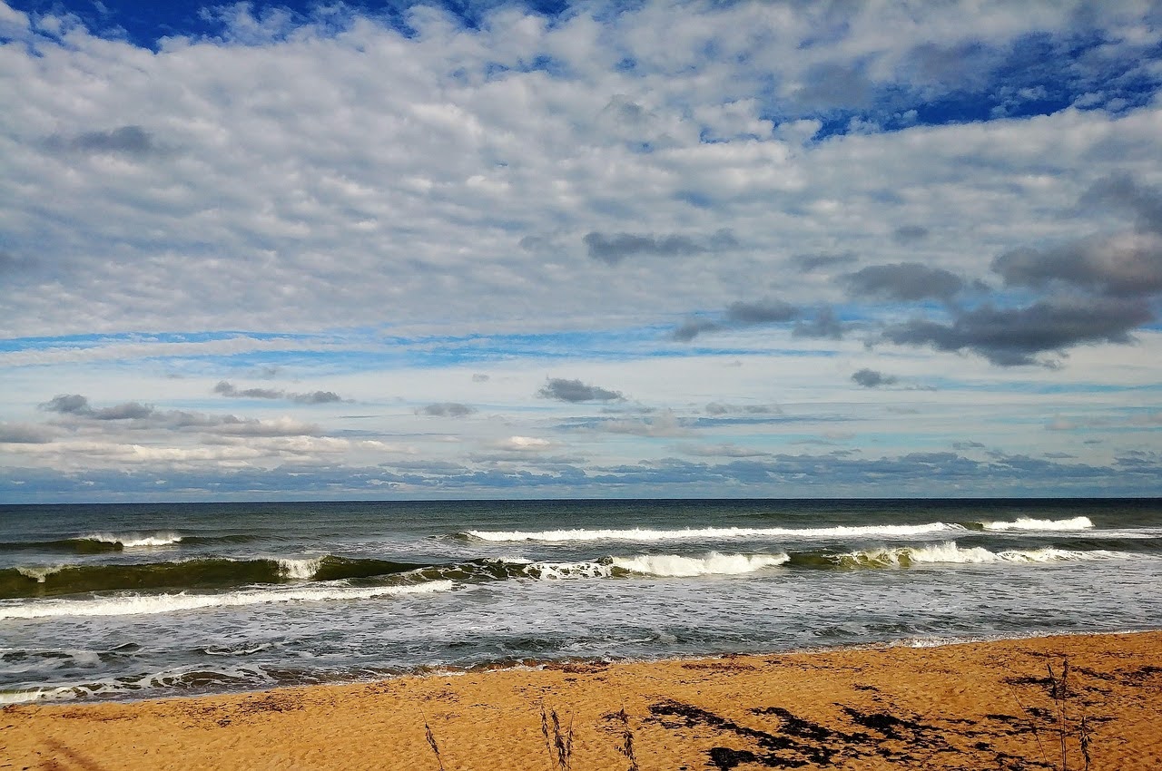 The image depicts a clear beach with rolling waves and a partially cloud sky.