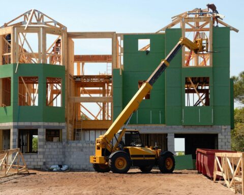 A construction vehicle waits in front of a partially constructed building with green and grey exteriors.