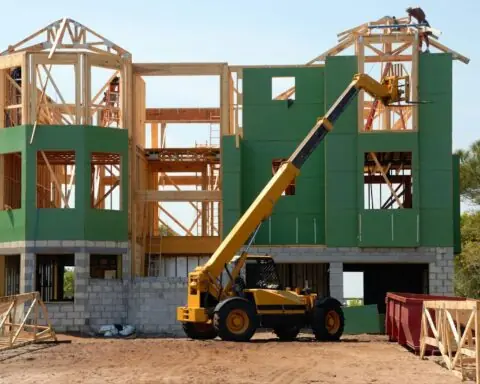 A construction vehicle waits in front of a partially constructed building with green and grey exteriors.