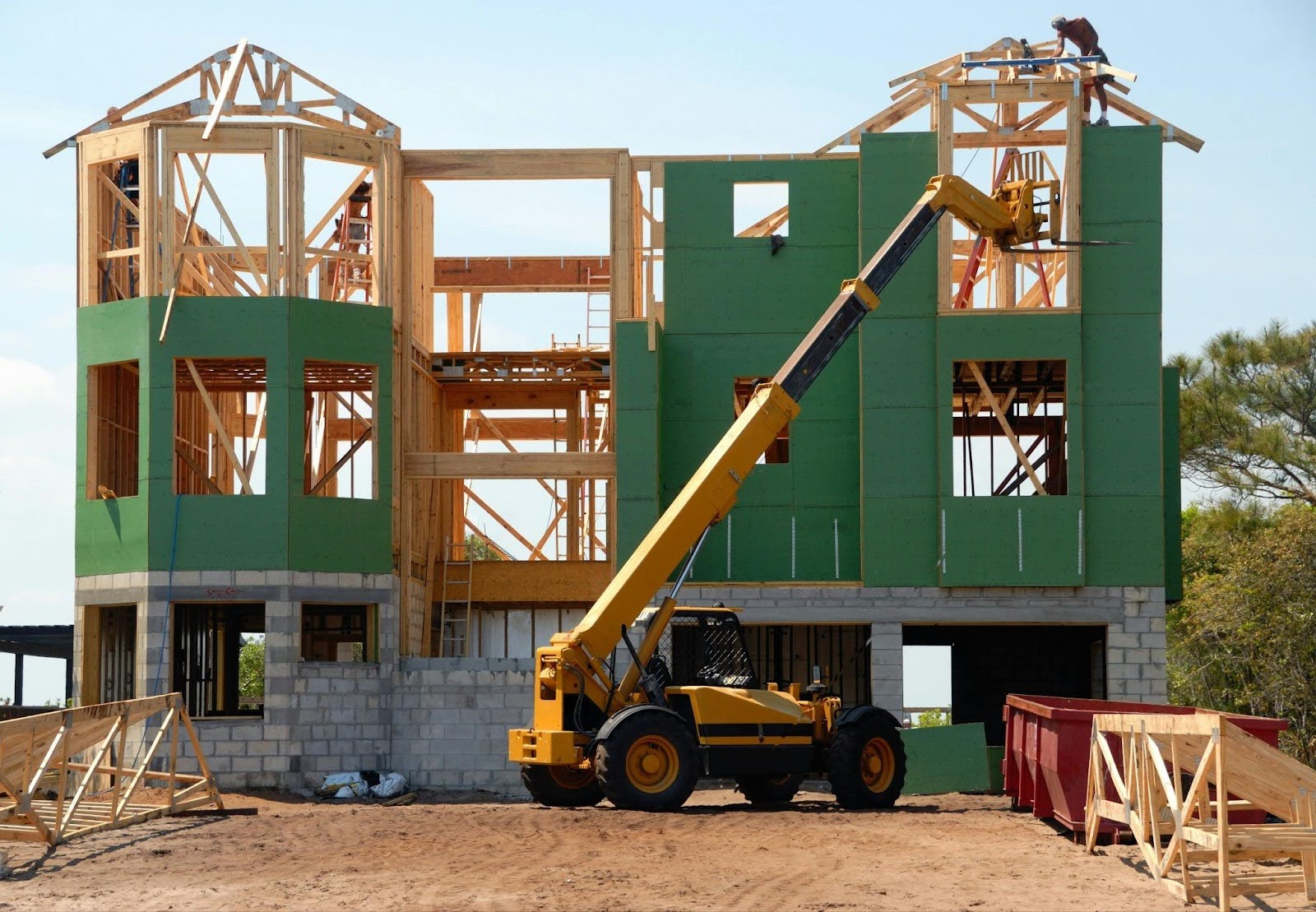 A construction vehicle waits in front of a partially constructed building with green and grey exteriors.