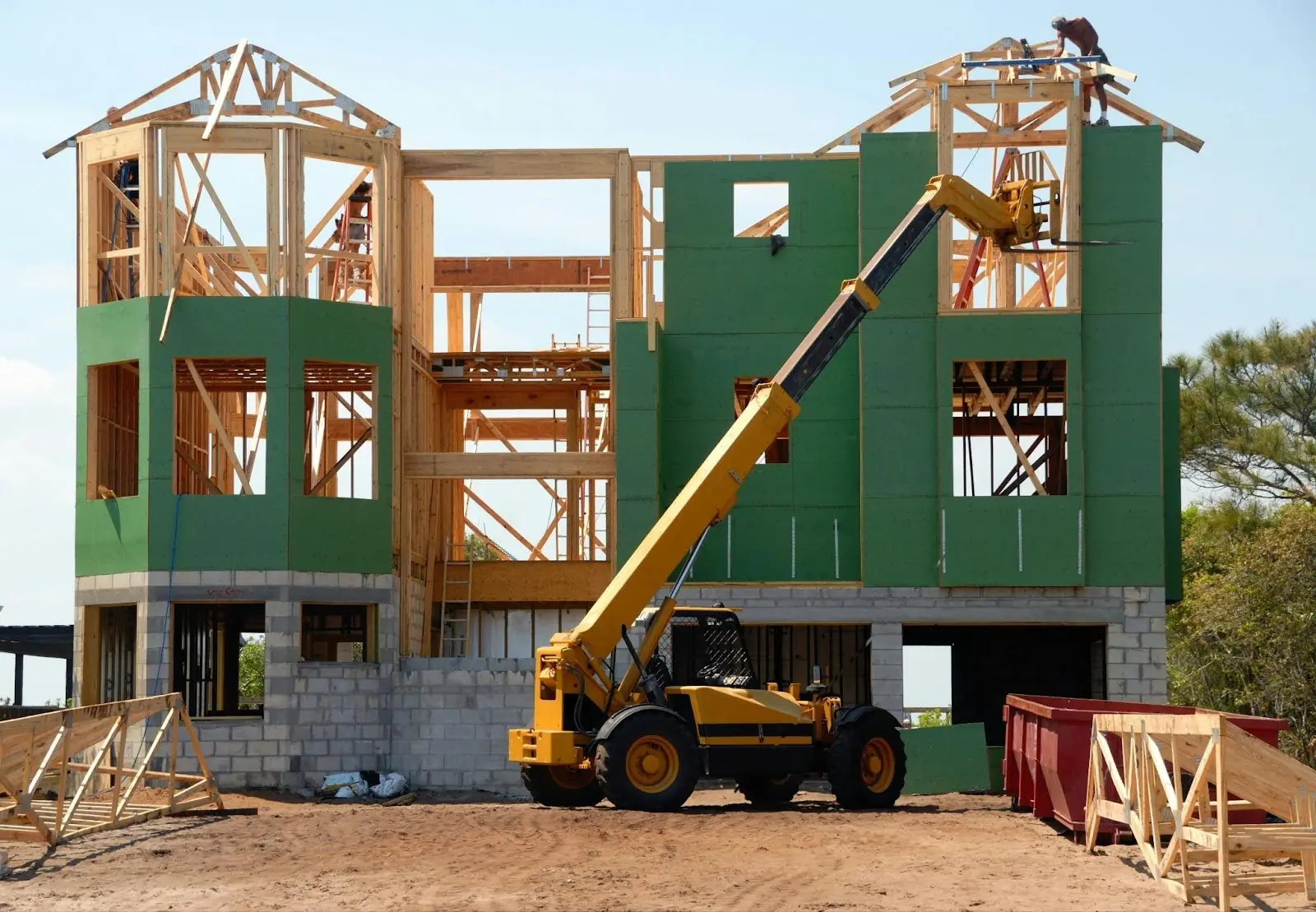 A construction vehicle waits in front of a partially constructed building with green and grey exteriors.