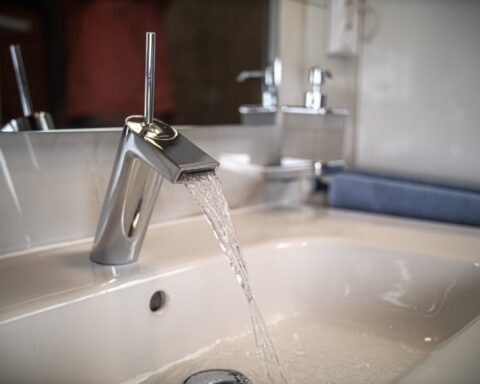 A water faucet pours water into a sink.