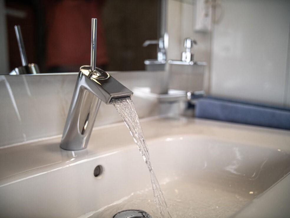 A water faucet pours water into a sink.