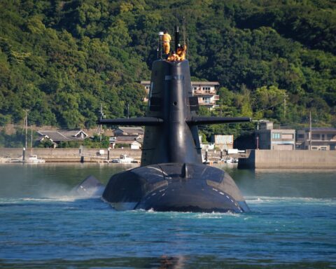 A submarine with crew on the top in the water before a grass landing.