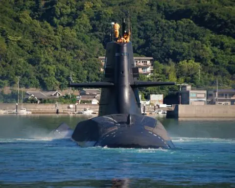 A submarine with crew on the top in the water before a grass landing.