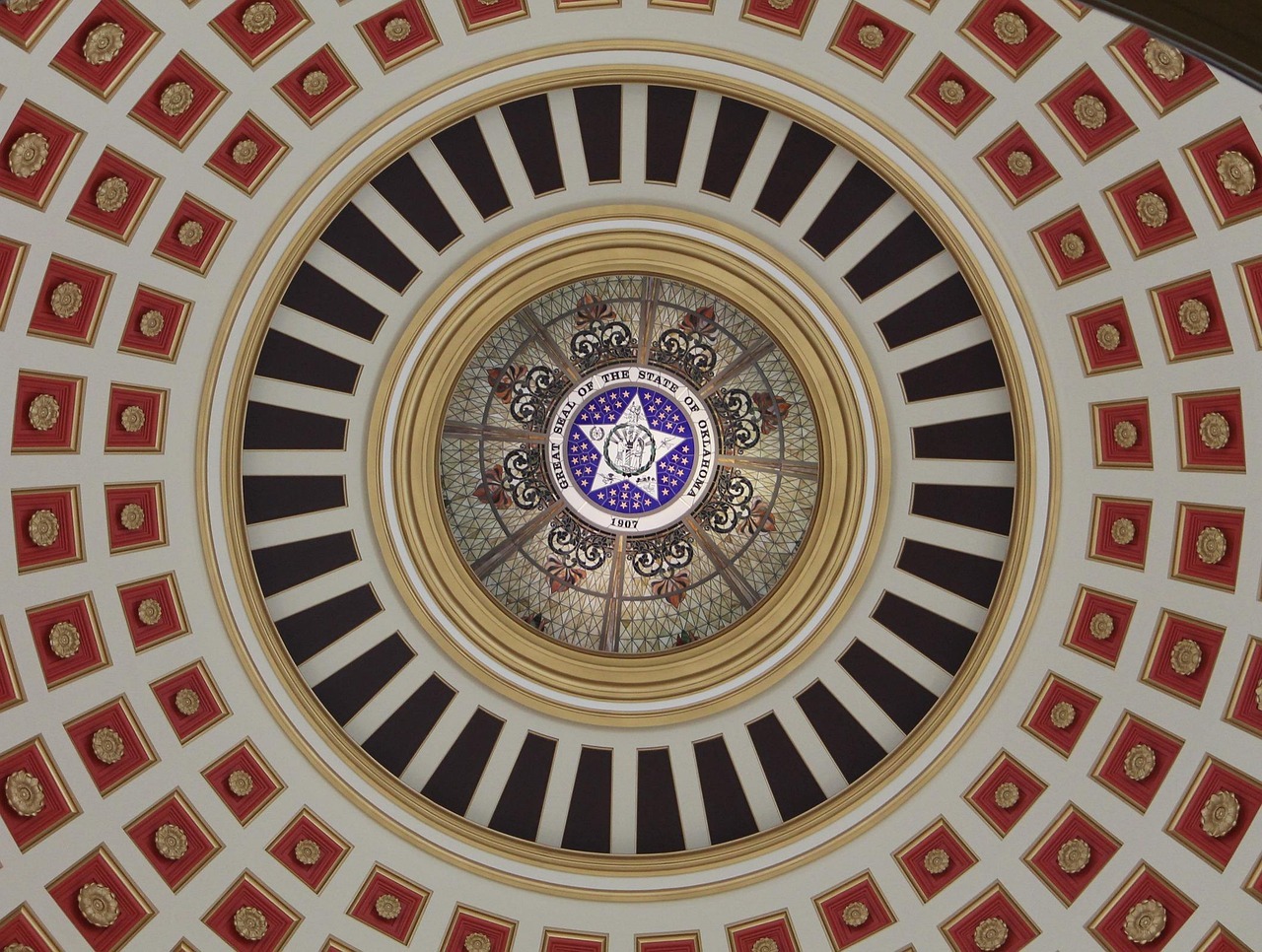 The Oklahoma seal is depicted within an artistic pattern outward with gold, red, black and white hues.