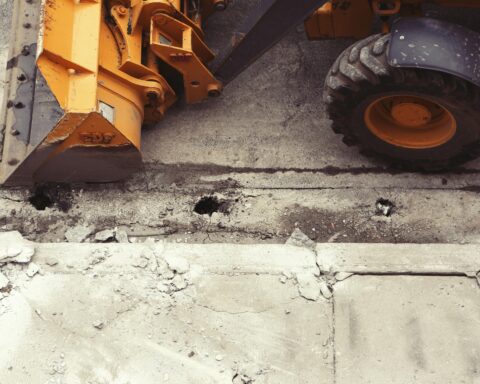 A yellow construction vehicle along a broken, crumbling sidewalk.