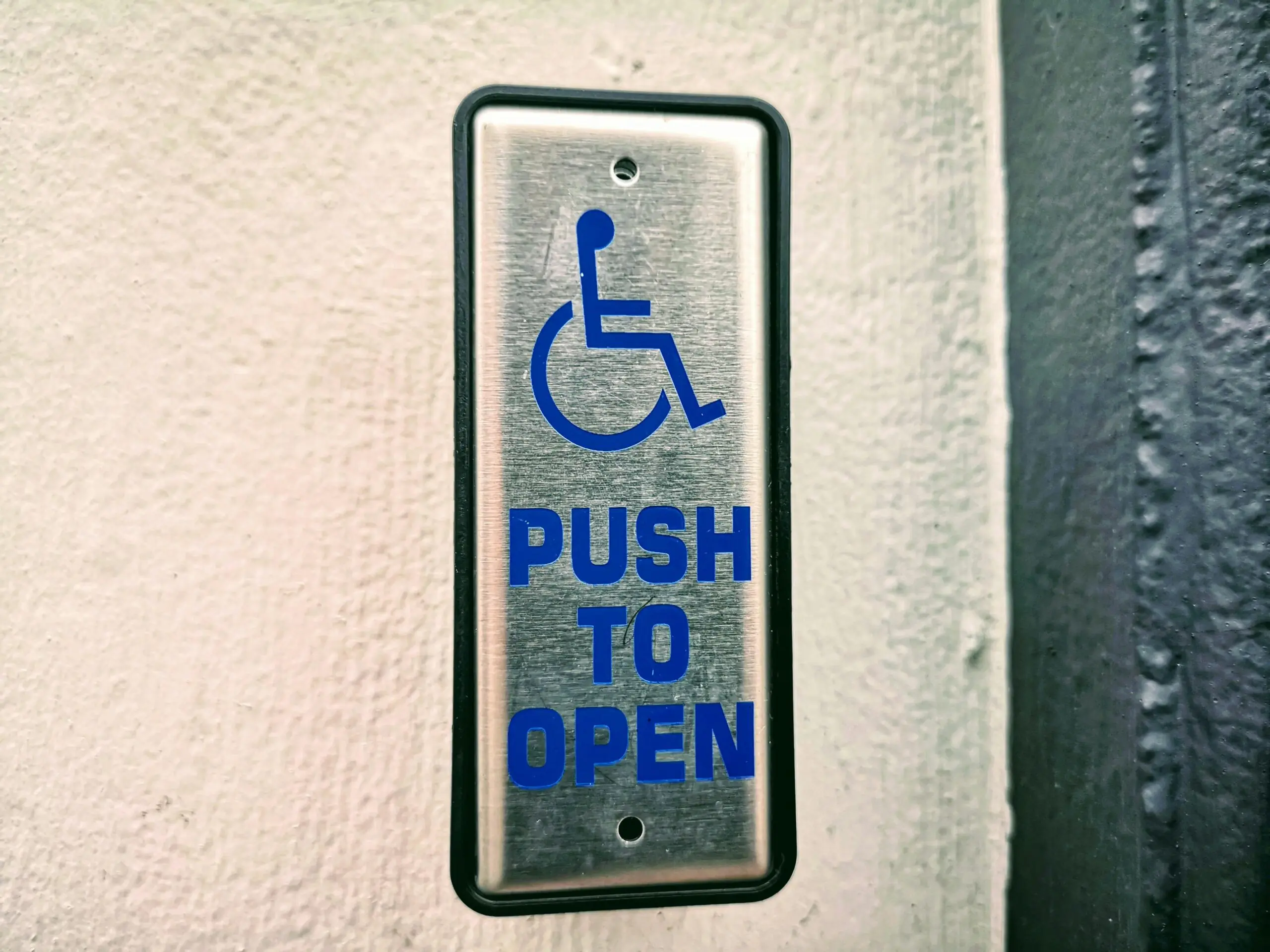 An accessibility button on a wall indicating that if one were to push the button, a door would open.