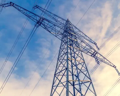 A transmission line from the ground before a cloudy blue sky.