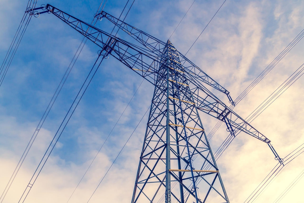 A transmission line from the ground before a cloudy blue sky.