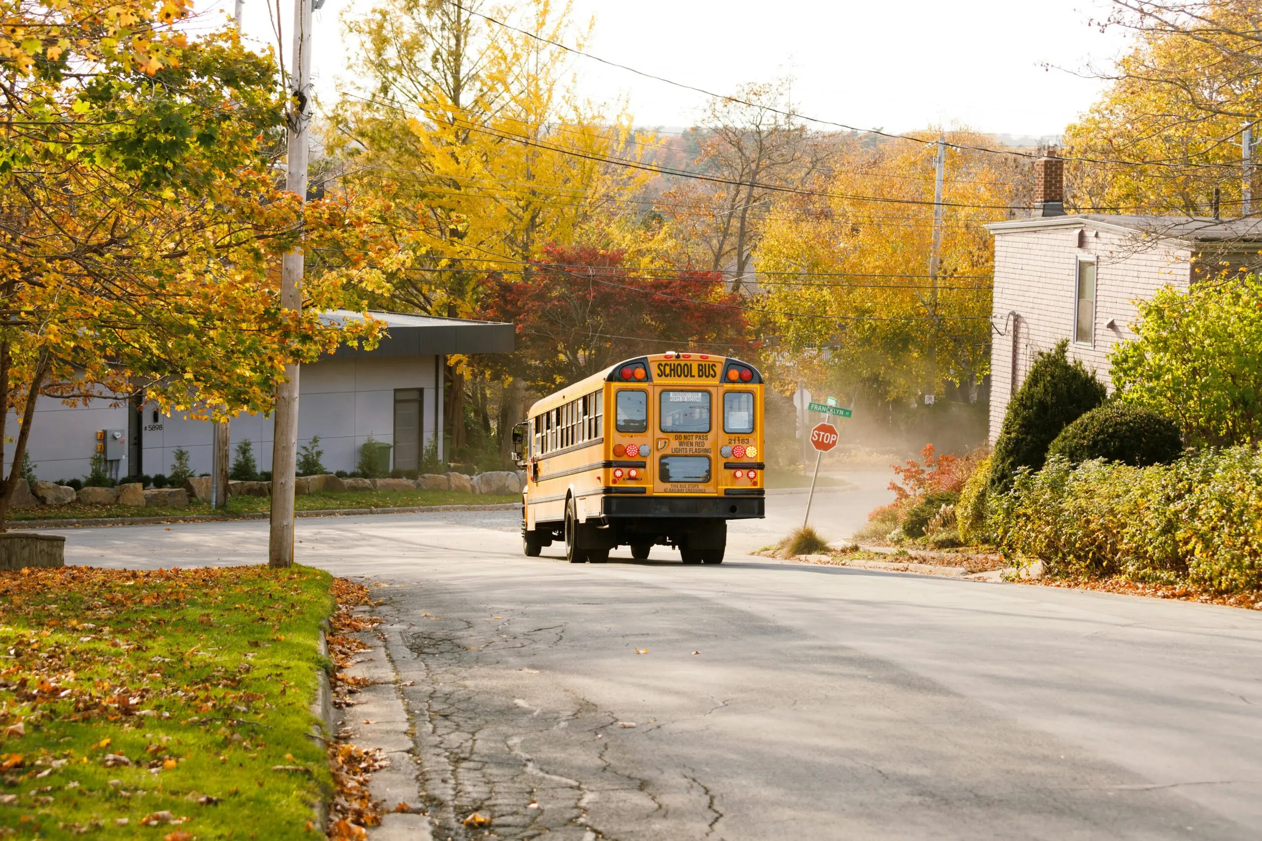 A yellow school bus at a stop sign on a road alongside grass, sidewalks and trees.
