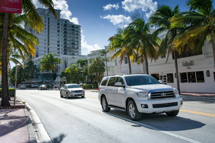 Two cars on a Florida road surrounded by buildings and palm trees.