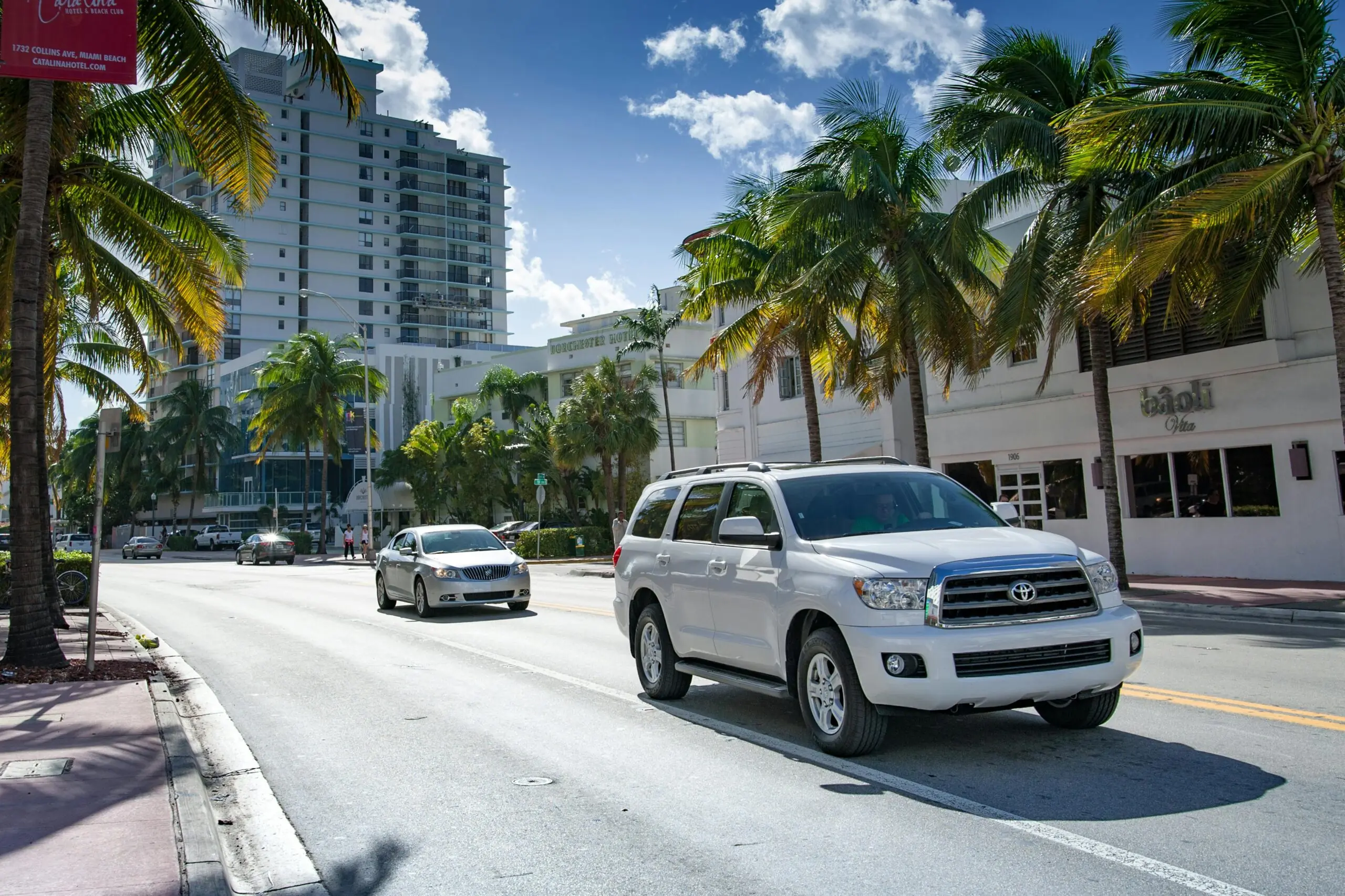 Two cars on a Florida road surrounded by buildings and palm trees.