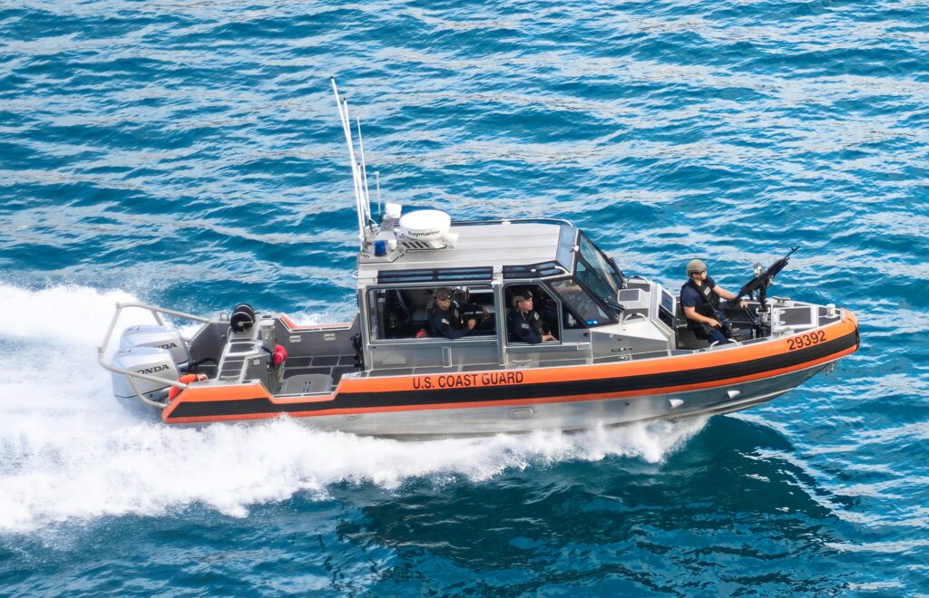 A Coast Guard boat armed with staff and a machine gun ride waves.