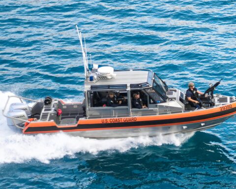 A Coast Guard boat armed with staff and a machine gun ride waves.