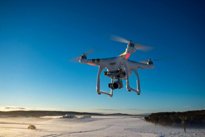 A drone in the air before a snow-dusted field and blue sky.