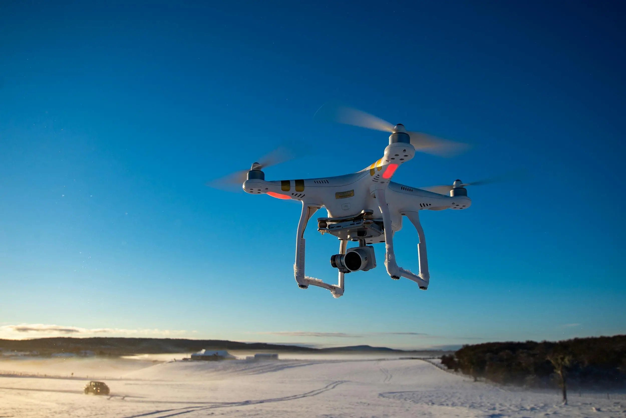 A drone in the air before a snow-dusted field and blue sky.
