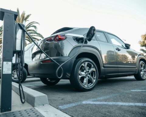 A grey electric vehicle is plugged into a chargin port outdoors.