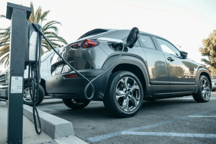 A grey electric vehicle is plugged into a chargin port outdoors.