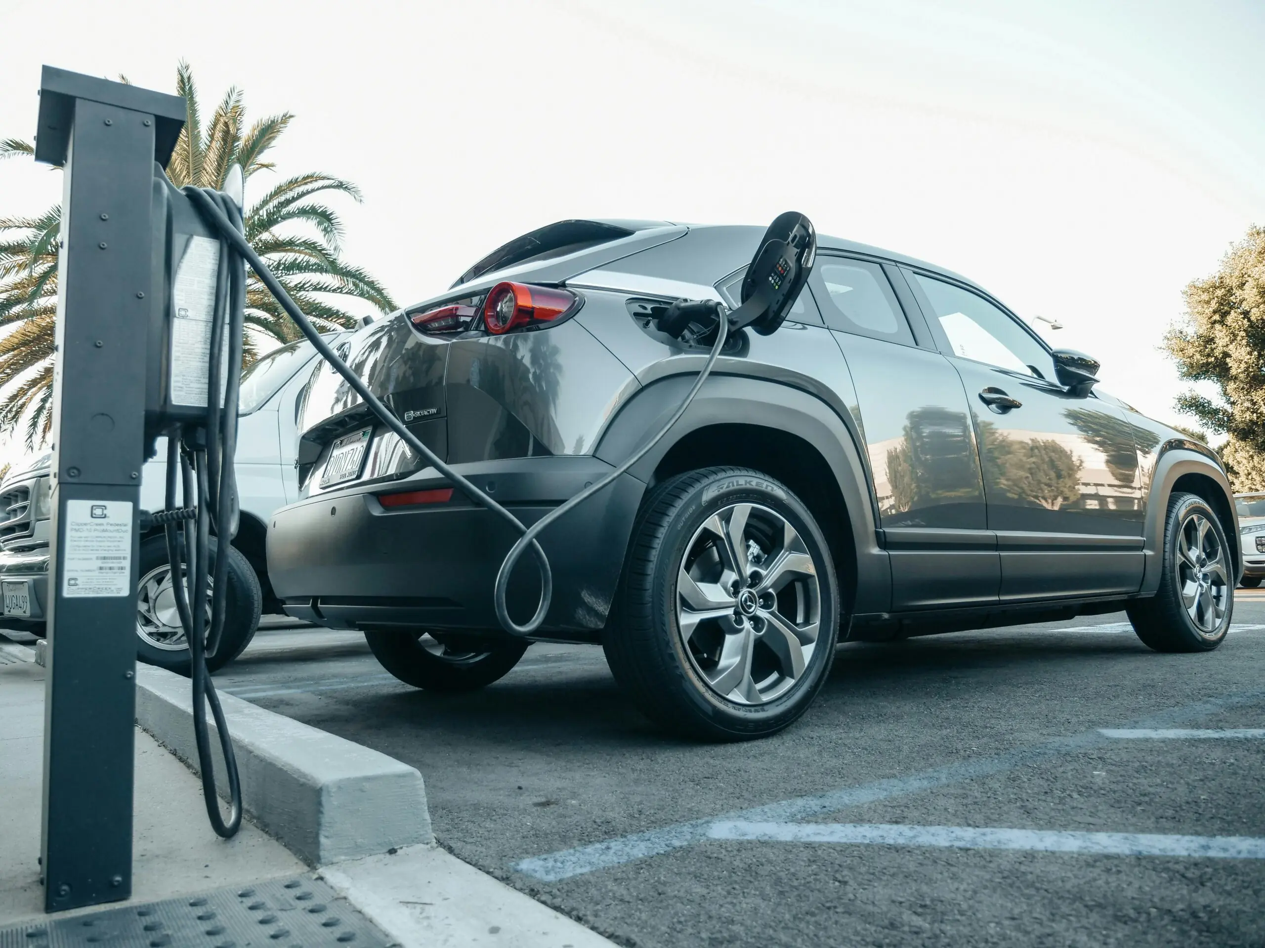 A grey electric vehicle is plugged into a chargin port outdoors.