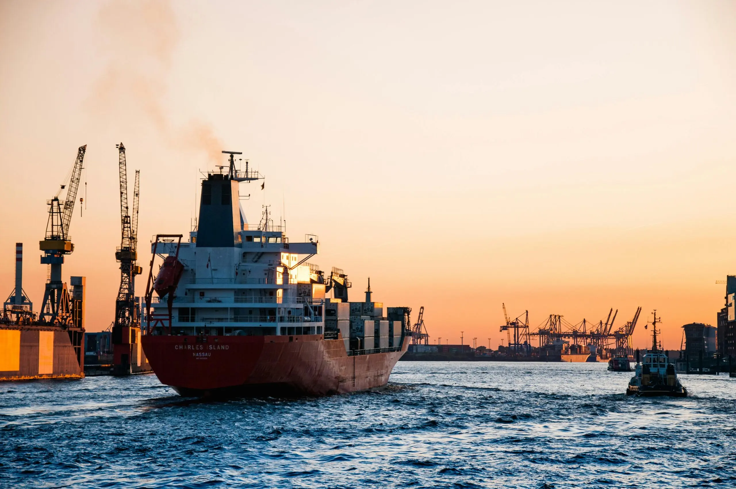 An ocean freightliner transports cargo along a navigable waterway under a setting sun-lit sky.