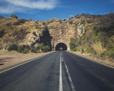 A highway leads to a tunnel within a hill carrying the road to the other side.