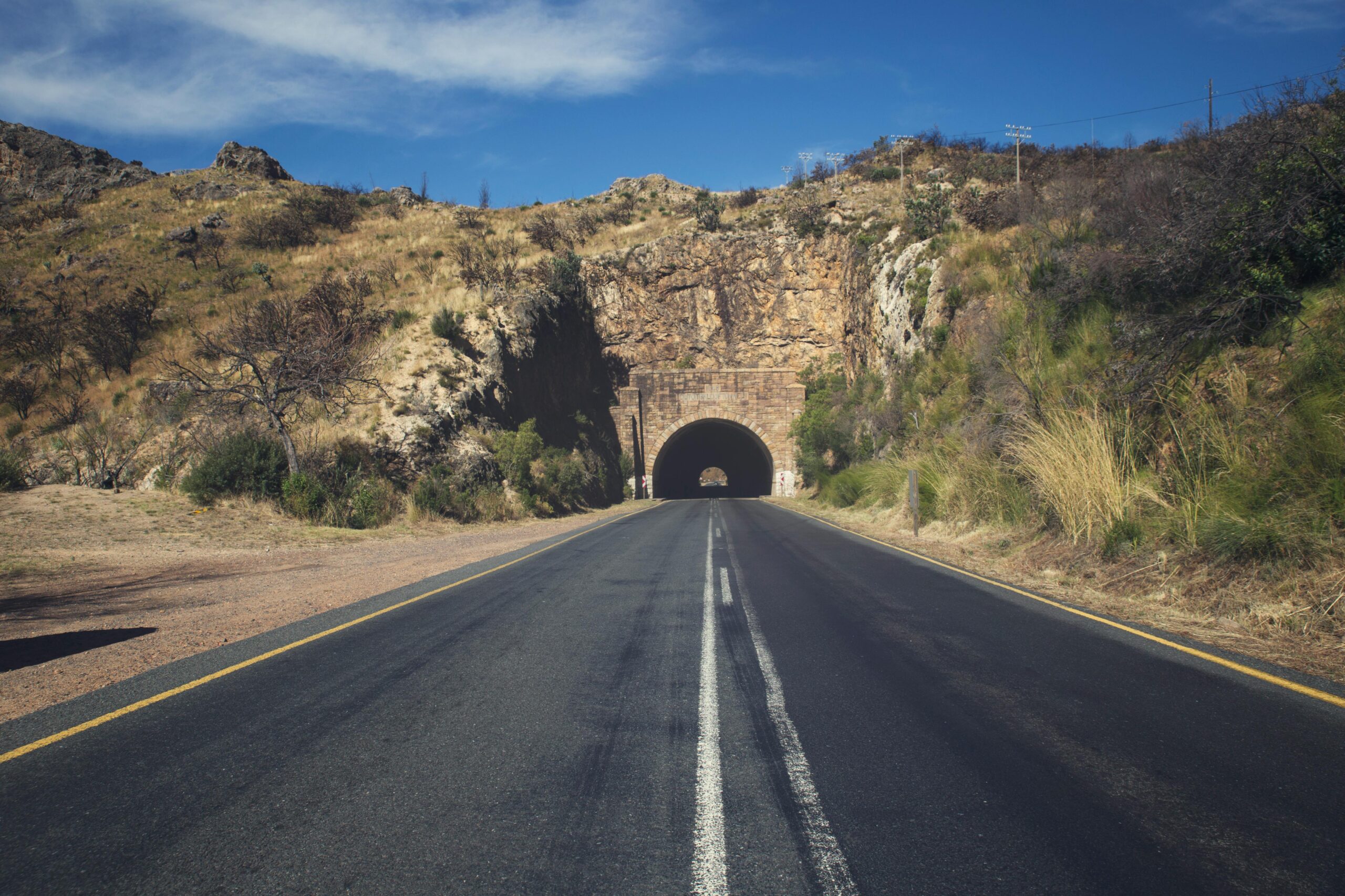 A highway leads to a tunnel within a hill carrying the road to the other side.