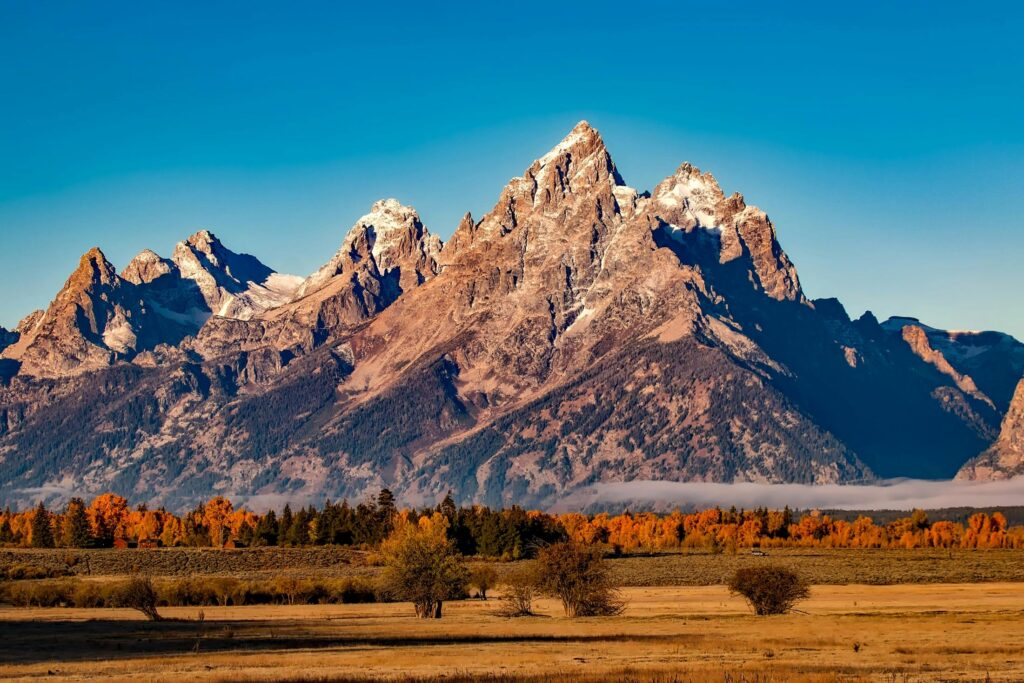 An American national park hosting a mountain range, flat grassy knolls and scattered dry-heat trees.