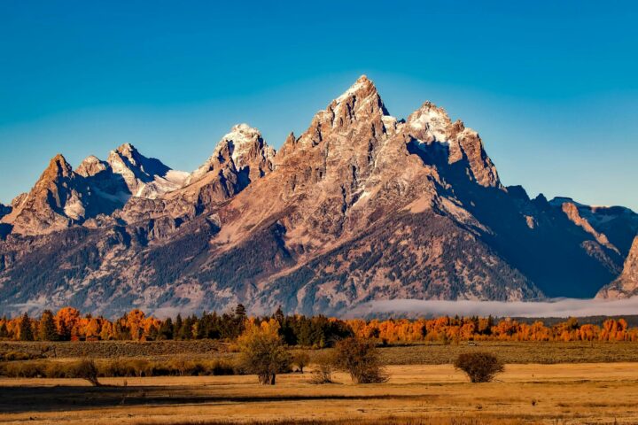 An American national park hosting a mountain range, flat grassy knolls and scattered dry-heat trees.