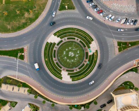An aerial shot of a roundabout with a fountain inside the middle and cars on the road.