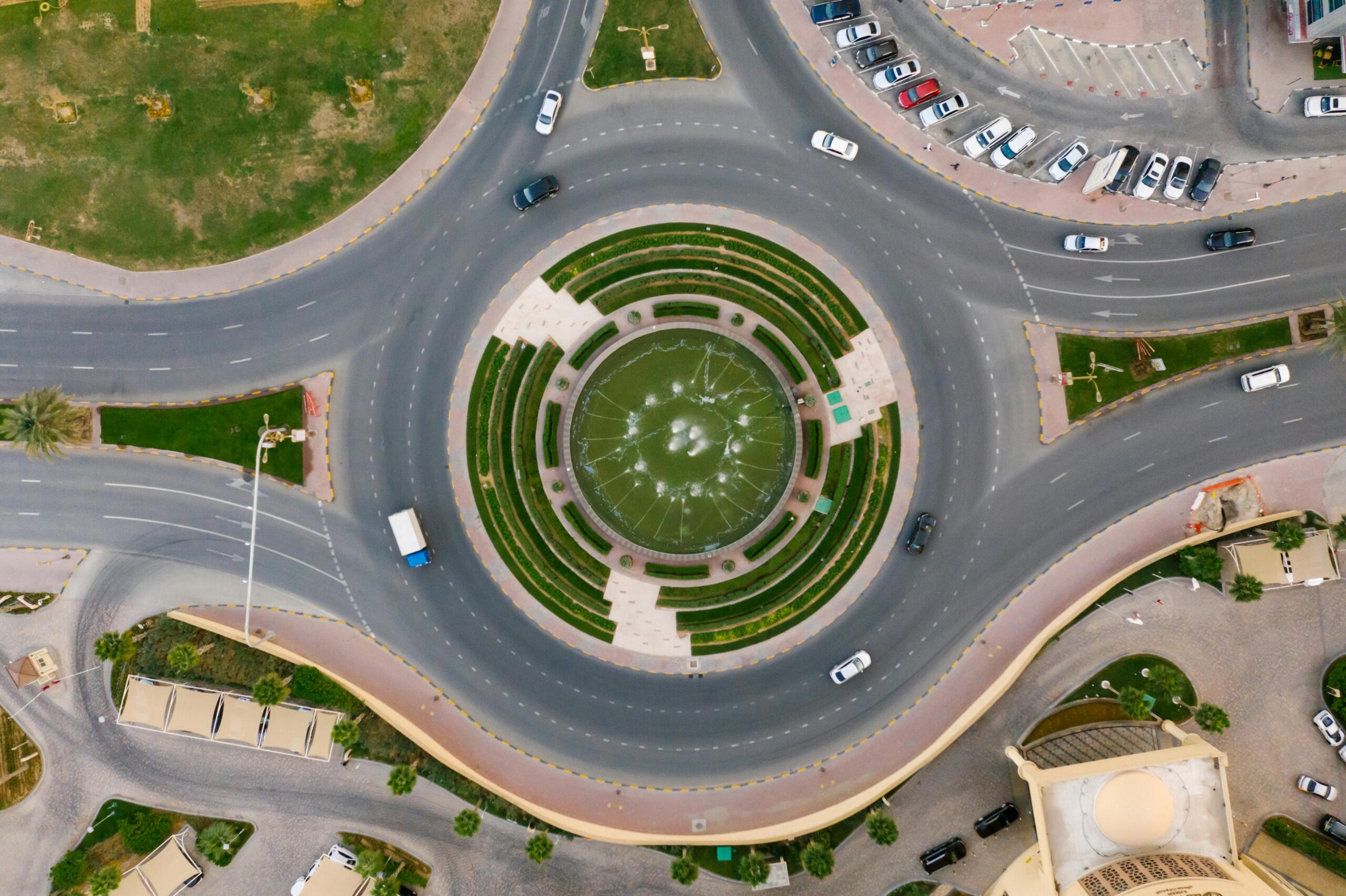 An aerial shot of a roundabout with a fountain inside the middle and cars on the road.
