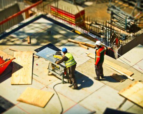 Builders work on a construction site standing on loose boards below.