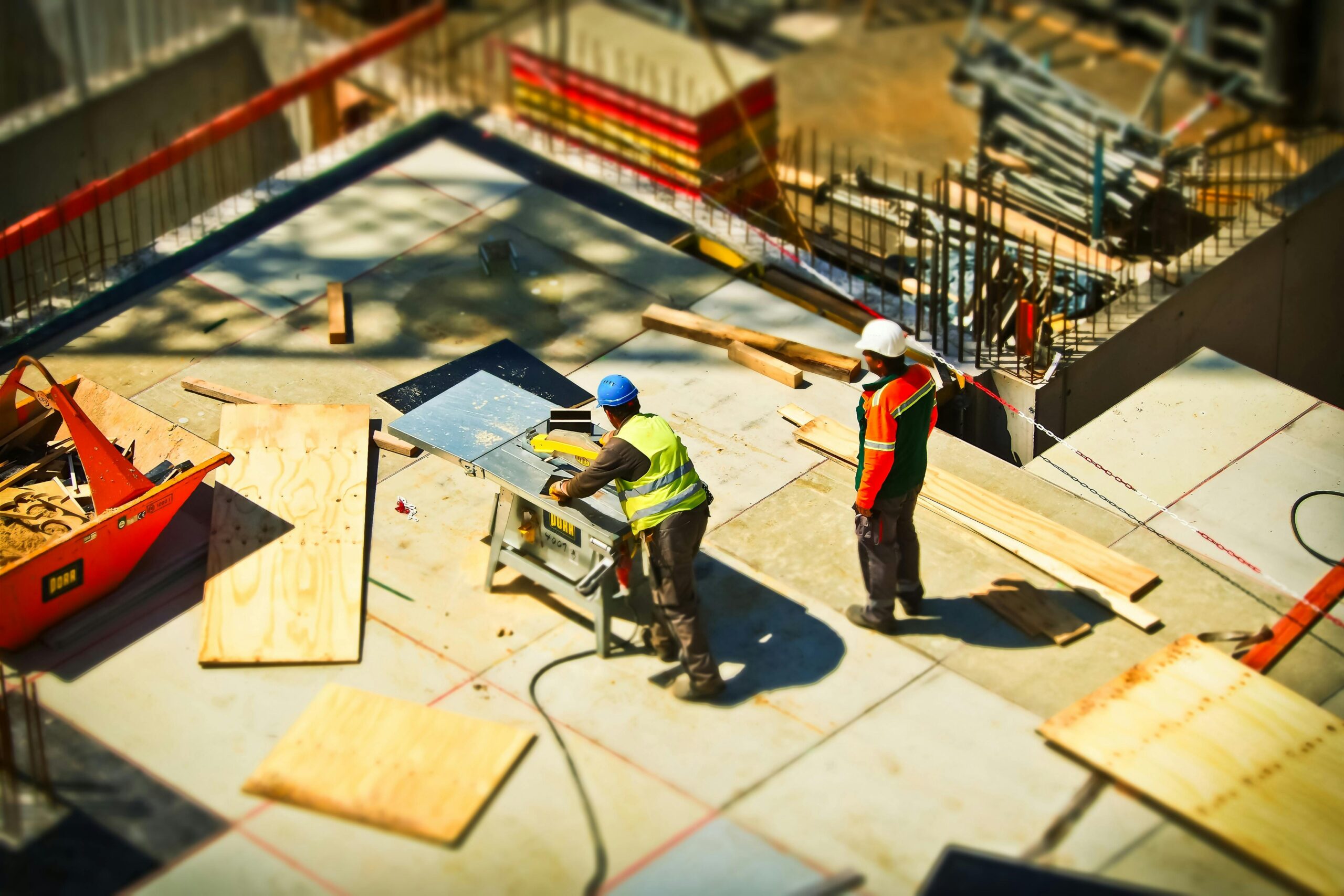 Builders work on a construction site standing on loose boards below.