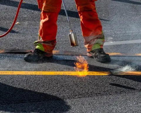 A construction worker ignites a blow torch to a road.