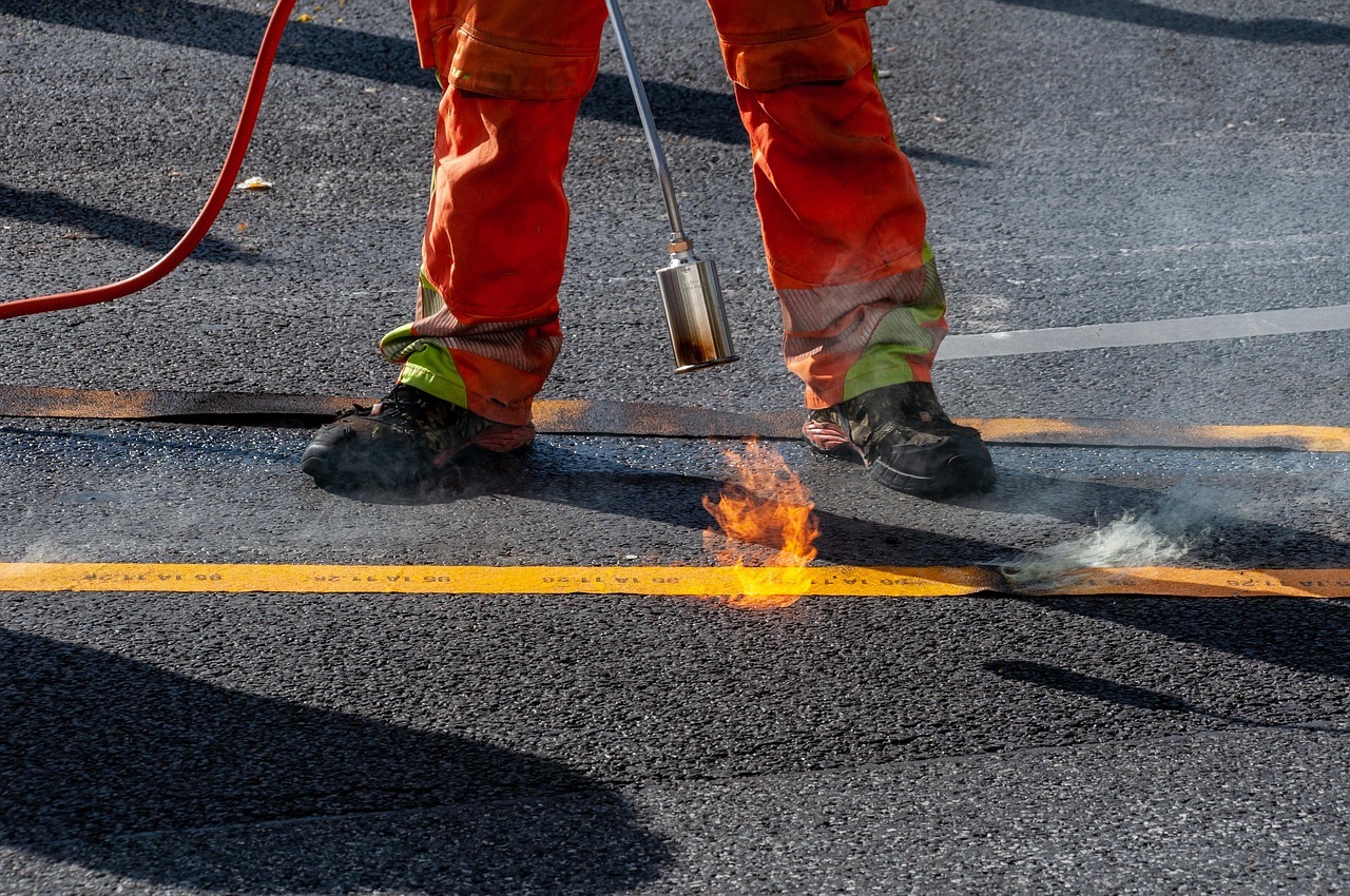A construction worker ignites a blow torch to a road.