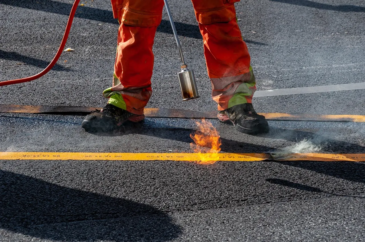 A construction worker ignites a blow torch to a road.