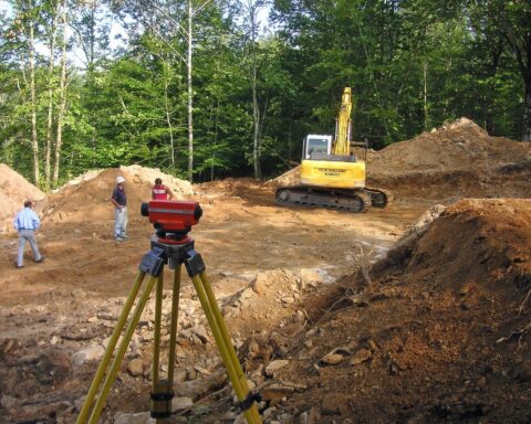 Construction workers, a land mover and surveying equipment prepare a site for potential development.