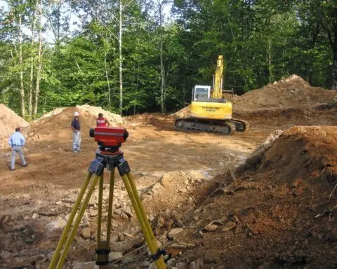 Construction workers, a land mover and surveying equipment prepare a site for potential development.