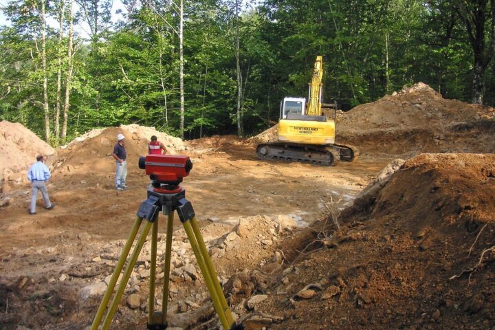 Construction workers, a land mover and surveying equipment prepare a site for potential development.