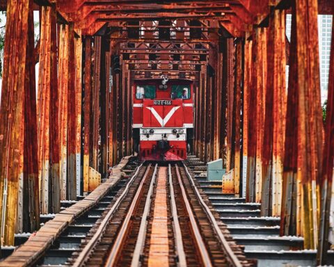 A train in the middle of a red, iron bridge.
