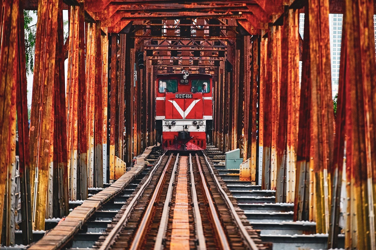 A train in the middle of a red, iron bridge.